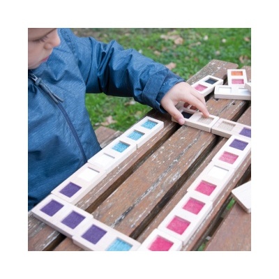 Criança a jogar dominós coloridos de madeira numa mesa ao ar livre