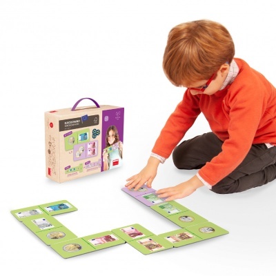 Menino a jogar com conjunto de jogo educativo em cartões verdes e caixa de papelão com alça roxa