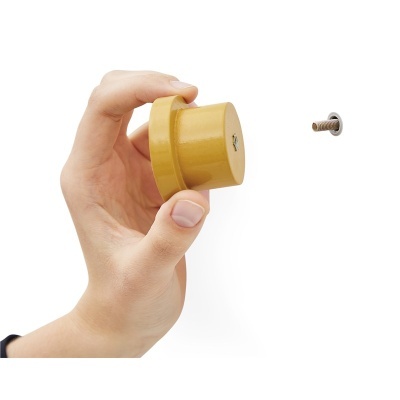 Mão segurando suporte amarelo redondo com parafuso e fixador na parede branca