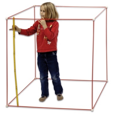 Menina dentro de estrutura cúbica vermelha segurando fita métrica amarela