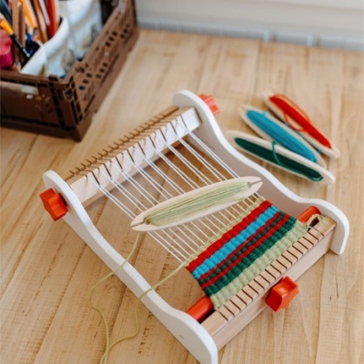 Tear de madeira com fios coloridos e fuso sobre mesa de madeira clara