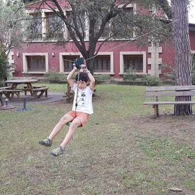 Criança numa tirolesa num jardim com bancos e edifício cor-de-rosa ao fundo