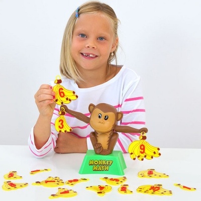 Miúda loira com camisola riscada a brincar com brinquedo de macaco e cachos de bananas numerados de plástico