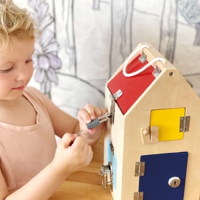 Criança loira a brincar com casa de madeira colorida com fechaduras e chaves