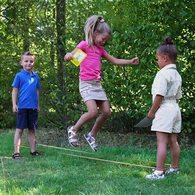 Três crianças a jogar com corda de saltar no jardim