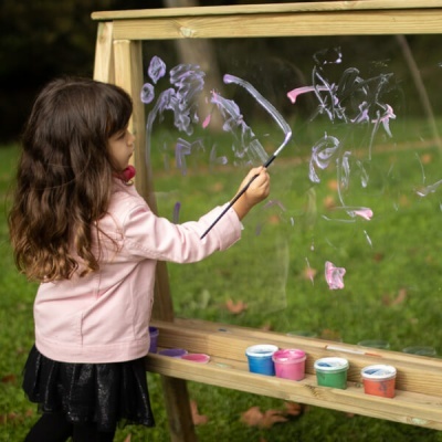 Menina a pintar em cavalete transparente com tintas coloridas ao ar livre