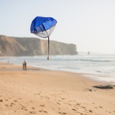 Paraquedas de brinquedo azul a ser lançado na praia ao lado do mar e penhascos