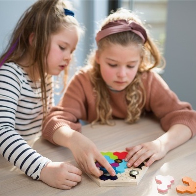 Quebra-cabeças hexagonal de madeira colorida com peças em várias cores manuseado por crianças