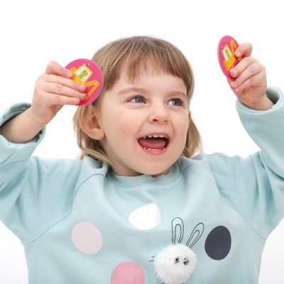 Menina sorridente com camisola azul clara com bolas coloridas e coelho, segurando objetos ovais rosas.