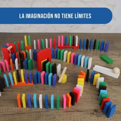 Peças de dominó coloridas em superfície de madeira com parede marmoreada e texto em espanhol.