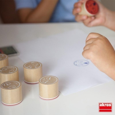 Carimbos de madeira com símbolos em papel branco e mãos de criança a carimbar.