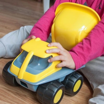 Brinquedo de carro amarelado com cinza e preto nas mãos de uma criança sentada