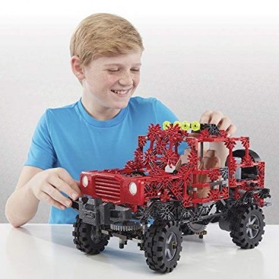 Menino loiro com camiseta azul brinca com jeep de construção vermelho e preto de peças encaixáveis sobre mesa branca