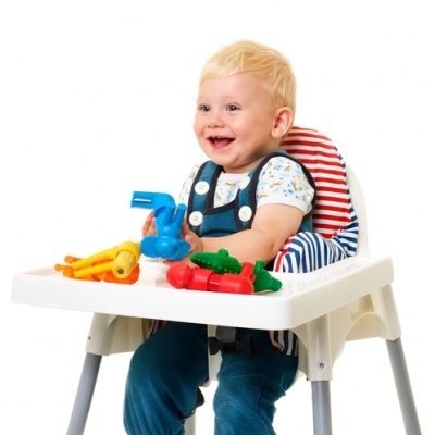 Bebé loiro numa cadeira alta branca a brincar com brinquedos coloridos