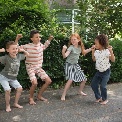 Quatro crianças descalças a posar de forma enérgica ao ar livre com roupa casual