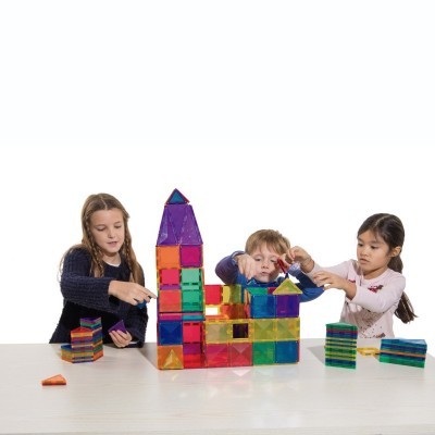 Três crianças a construir com blocos magnéticos coloridos e transparentes numa mesa branca