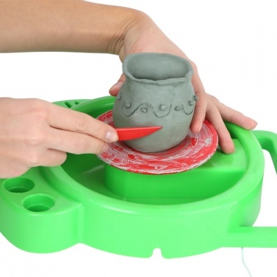 Mãos a modelar vaso de barro cinzento em tabuleiro verde com base giratória vermelha