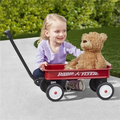 Menina sentada ao lado de carrinho vermelho Radio Flyer com urso de peluche