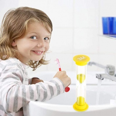 Relógio de areia amarelo na pia e criança a escovar os dentes