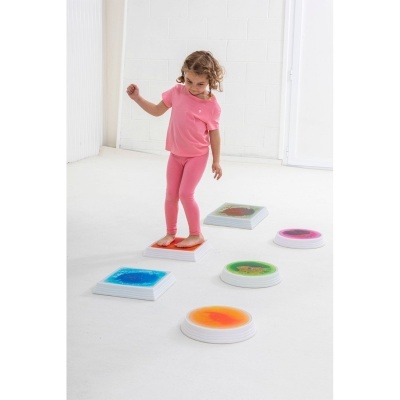 Criança em roupa cor-de-rosa com blocos sensoriais coloridos no chão