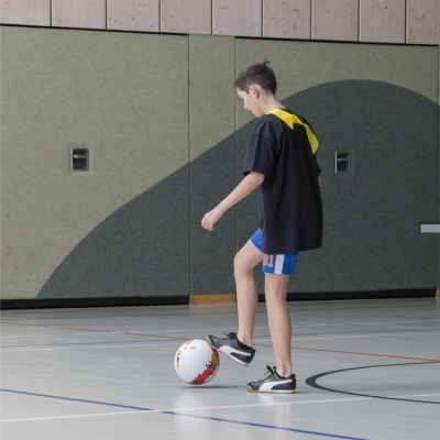 Menino a jogar futebol num ginásio com bola branca e calçado desportivo preto