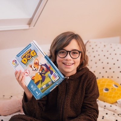Criança sorridente com óculos a segurar caixa do jogo SMART DOG FUN
