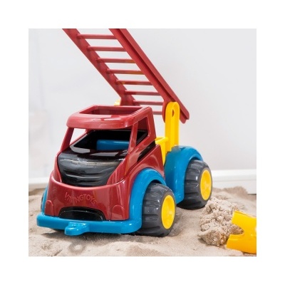 Caminhão de brinquedo de bombeiros em plástico colorido na areia com pá amarela