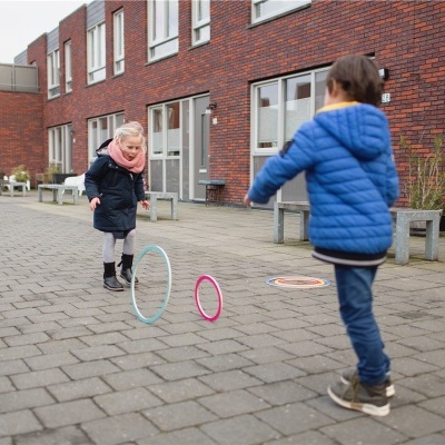 Crianças a jogar com aros coloridos num passadiço em frente a prédios residenciais de tijolos vermelhos