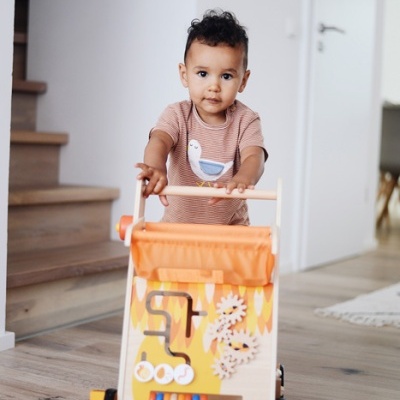 Criança a empurrar um andador de madeira com actividades lúdicas coloridas