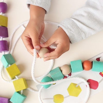 Cordão de contas coloridas de madeira para encaixe com criança a brincar