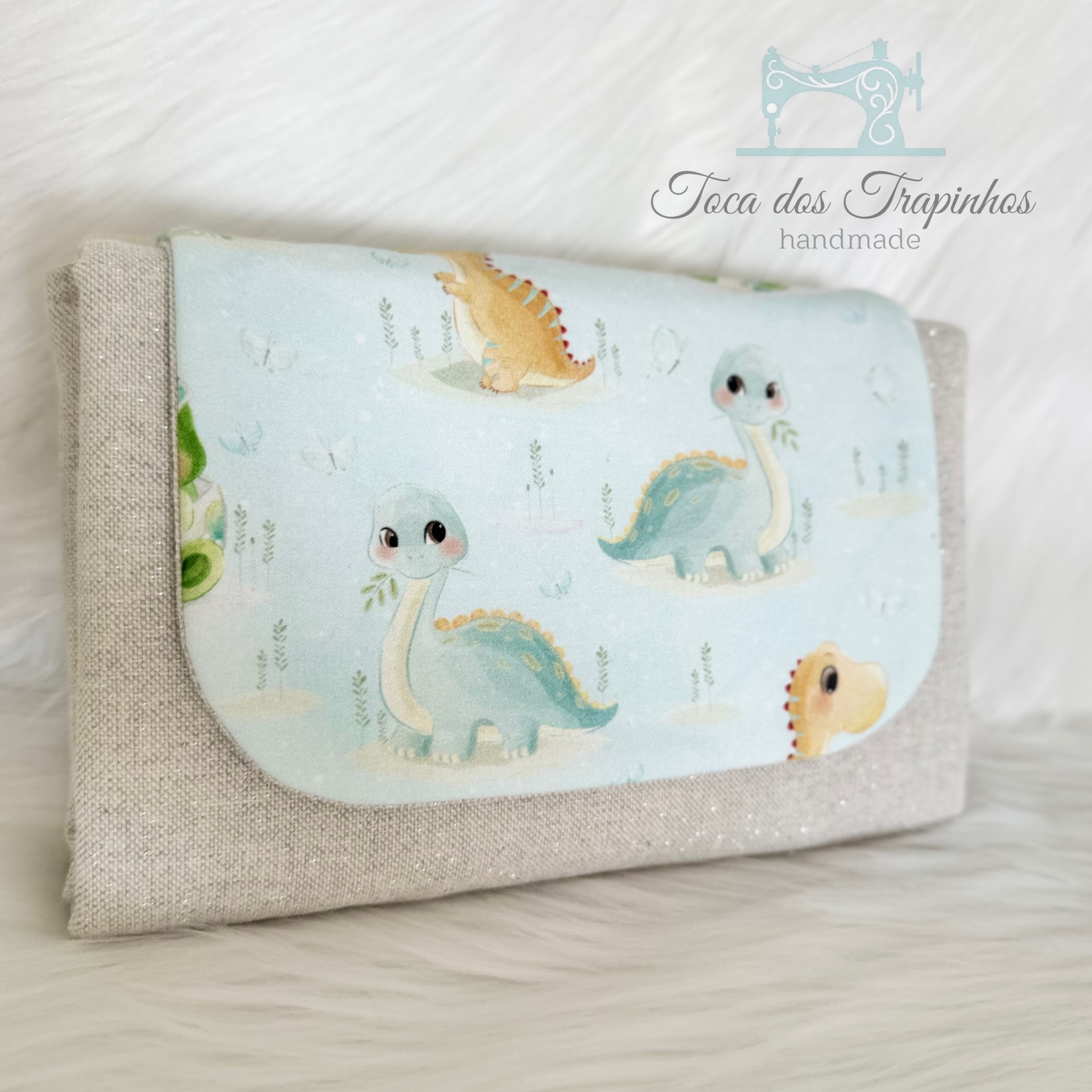 Carteira bege com aba azul claro estampada com dinossauros pastel.
