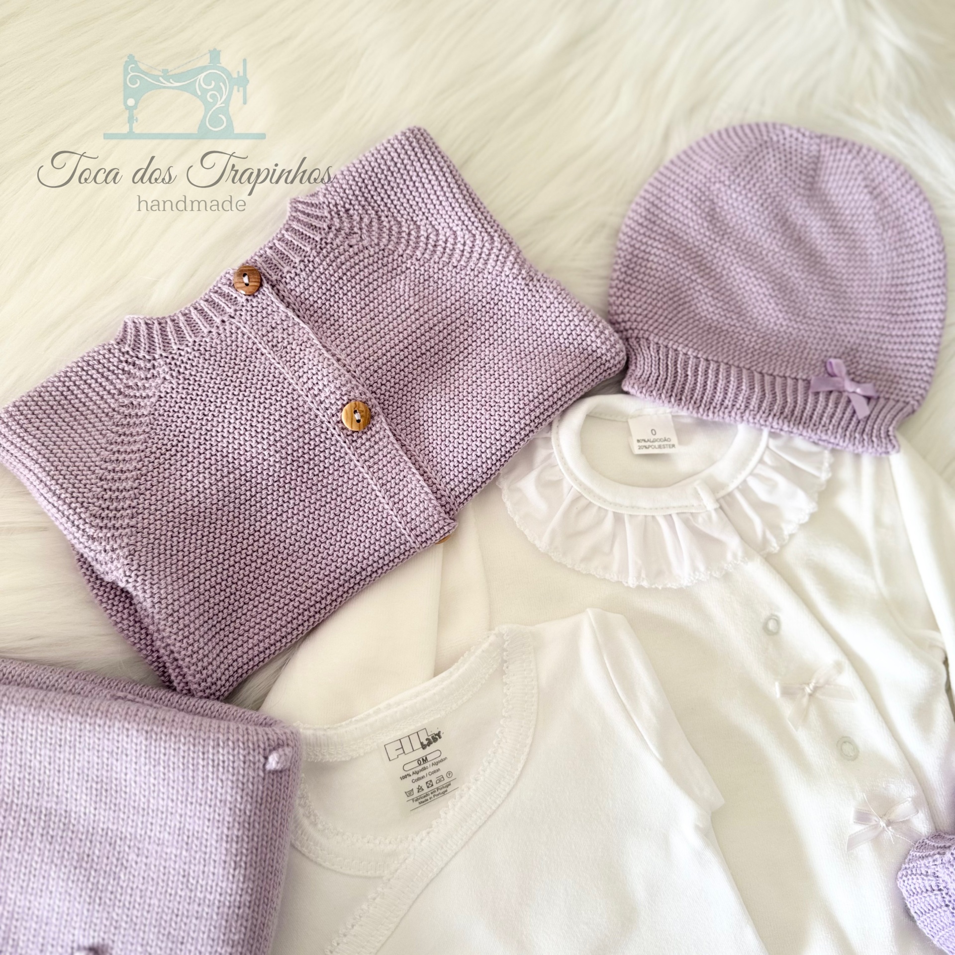 Conjunto de roupa de bebé lilás e branco sobre manta de pelo branco
