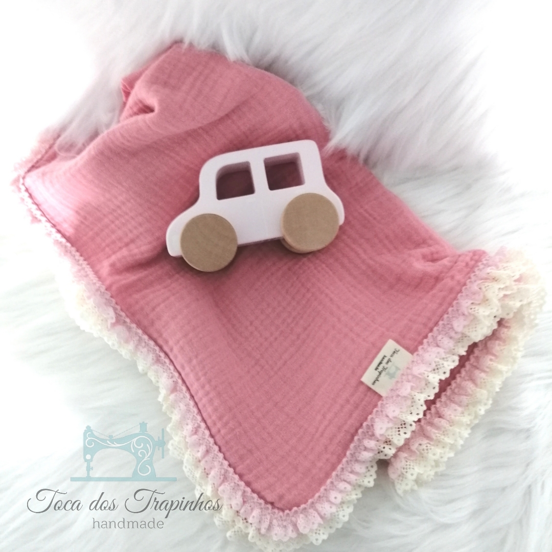 Manta rosa com borda rendada e carro de madeira branco sobre fundo branco felpudo