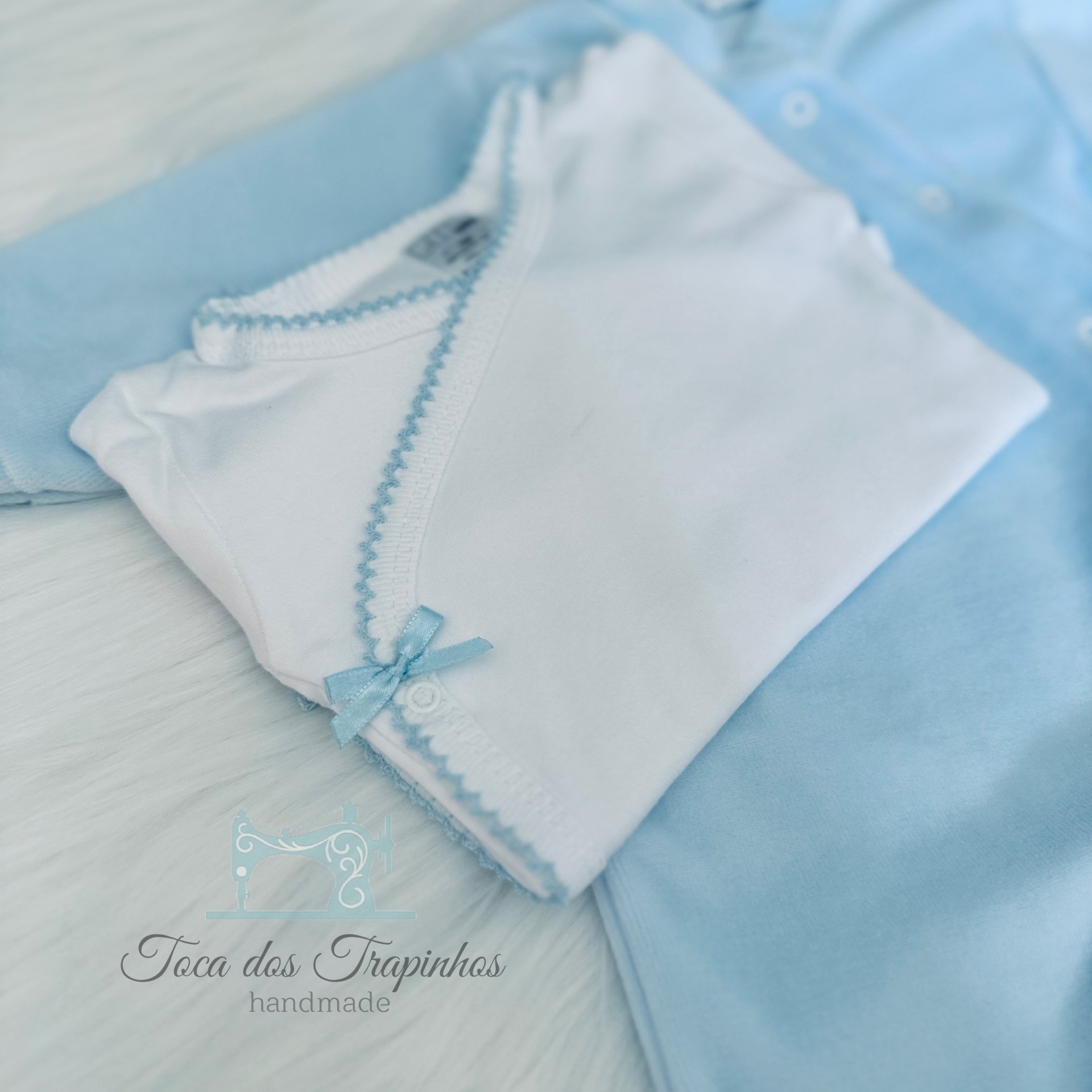 Conjunto de roupa de bebé branca e azul clara com detalhes em fita e ponto zig-zag