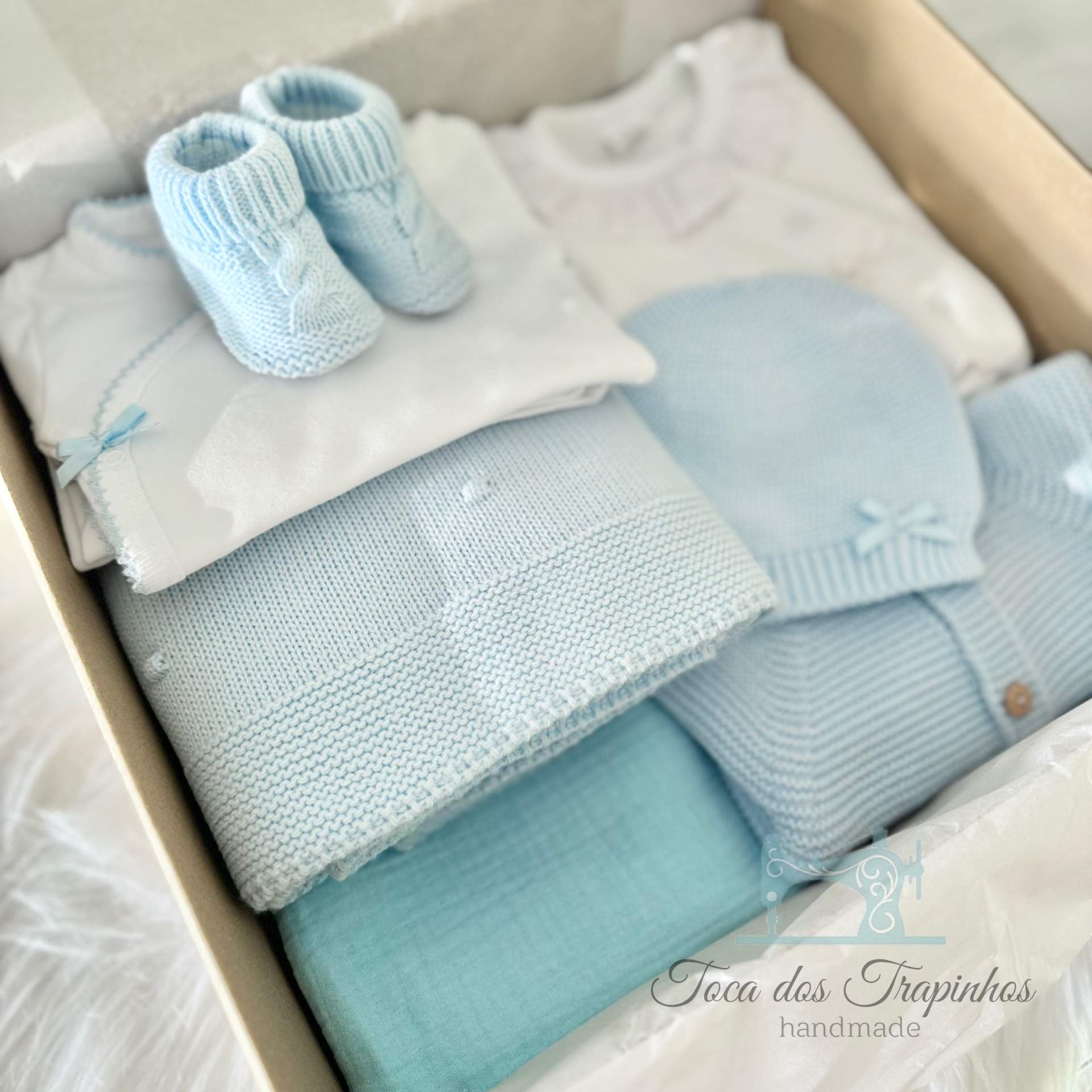 Conjunto de roupinhas e acessórios de bebé em azul claro e branco, prontos para oferta.