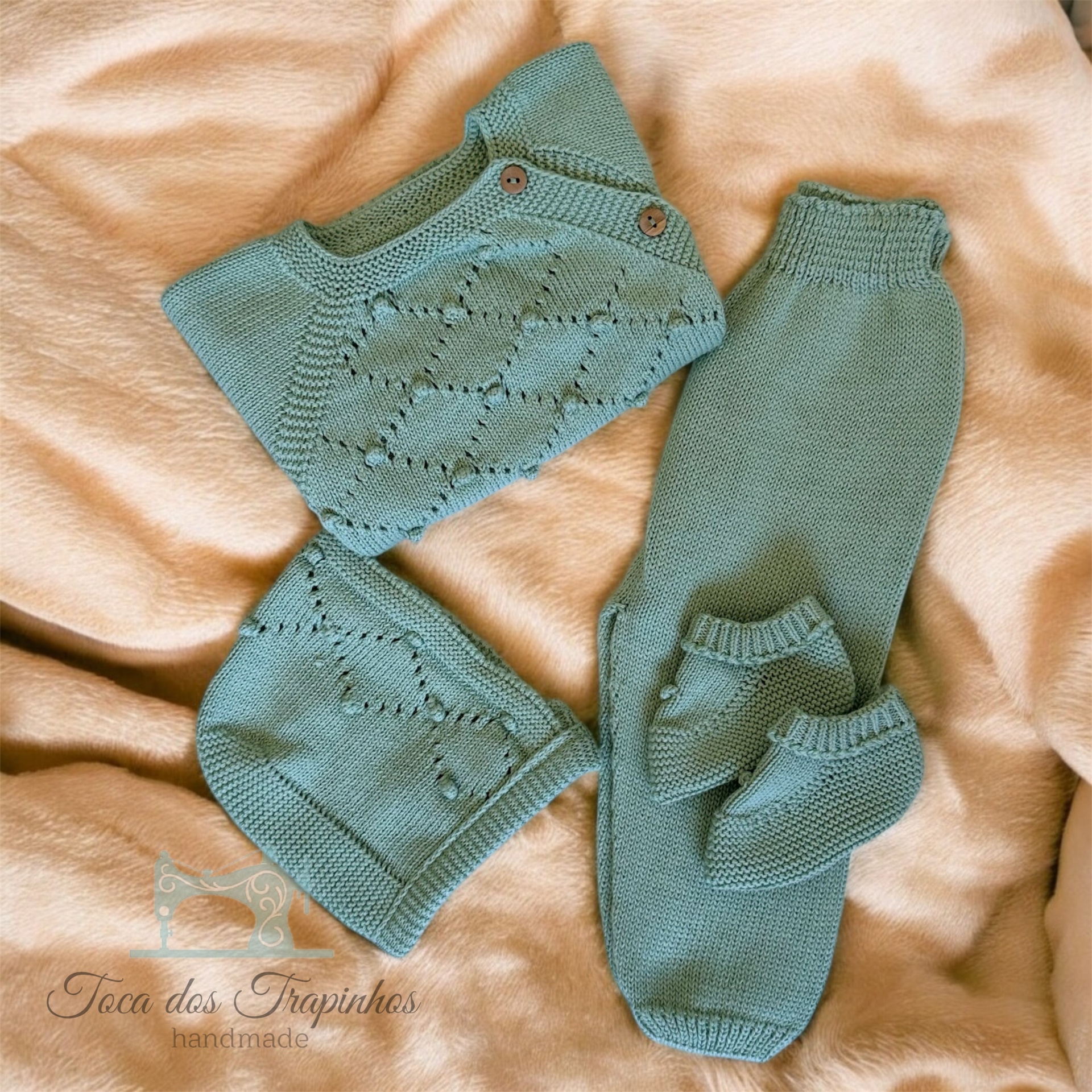 Conjunto de roupa de bebé em malha verde-água composto por camisola, calças, touca e pantufas sobre fundo castanho claro