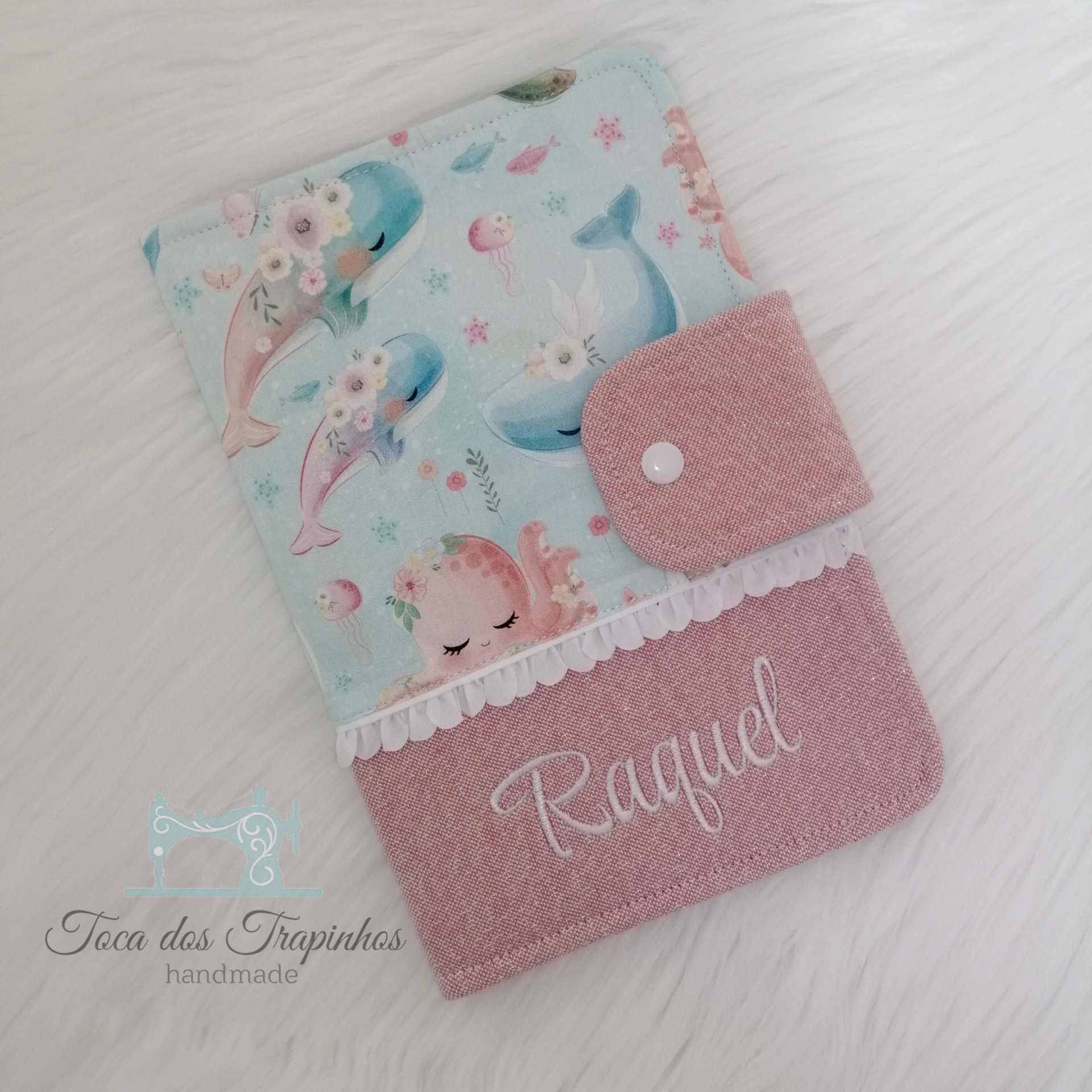 Capa para caderno em tecidos rosa e azul claro com desenhos de animais marinhos e nome Raquel