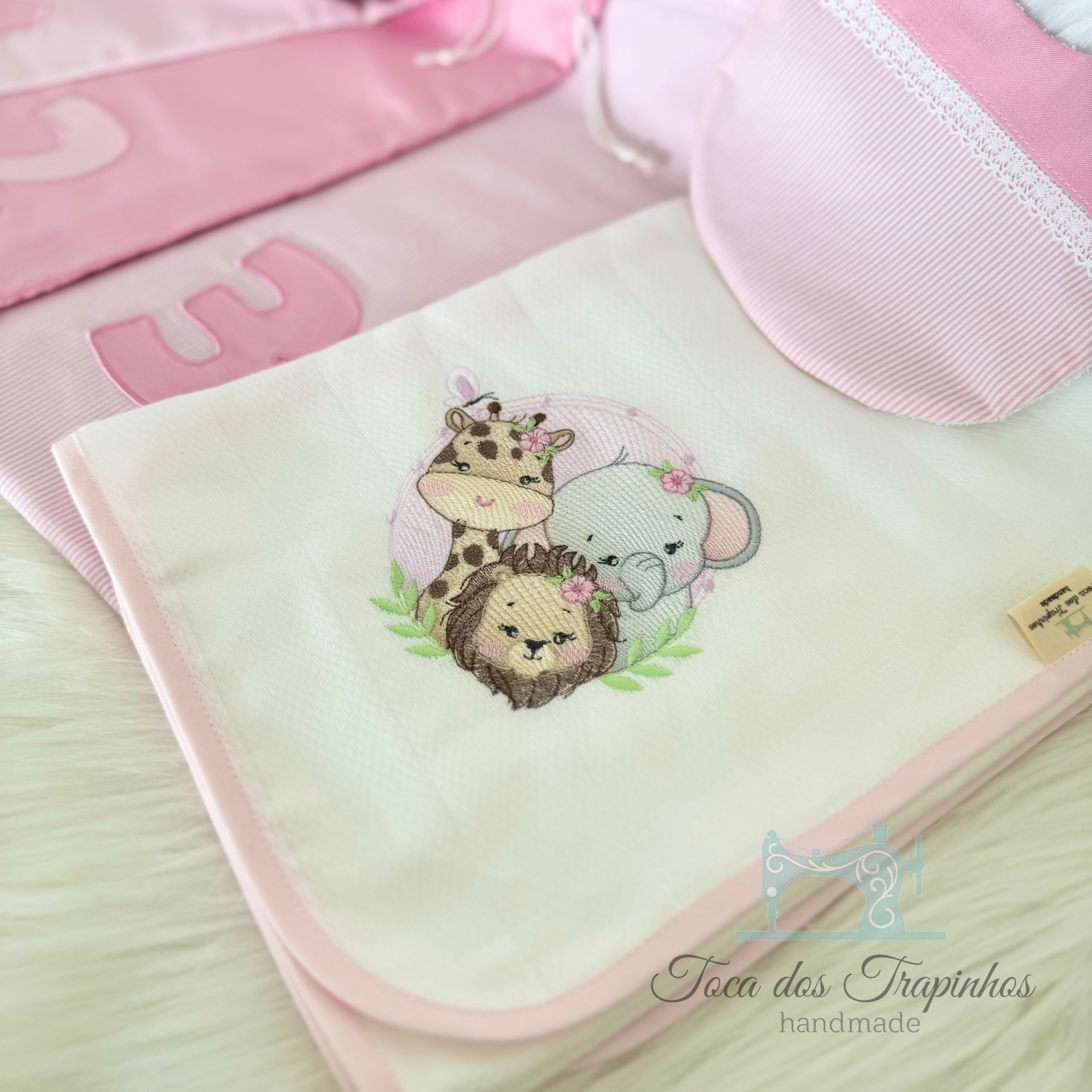 Toalha branca com bordado de girafa, leão e elefante e tecido rosa com números aplicados