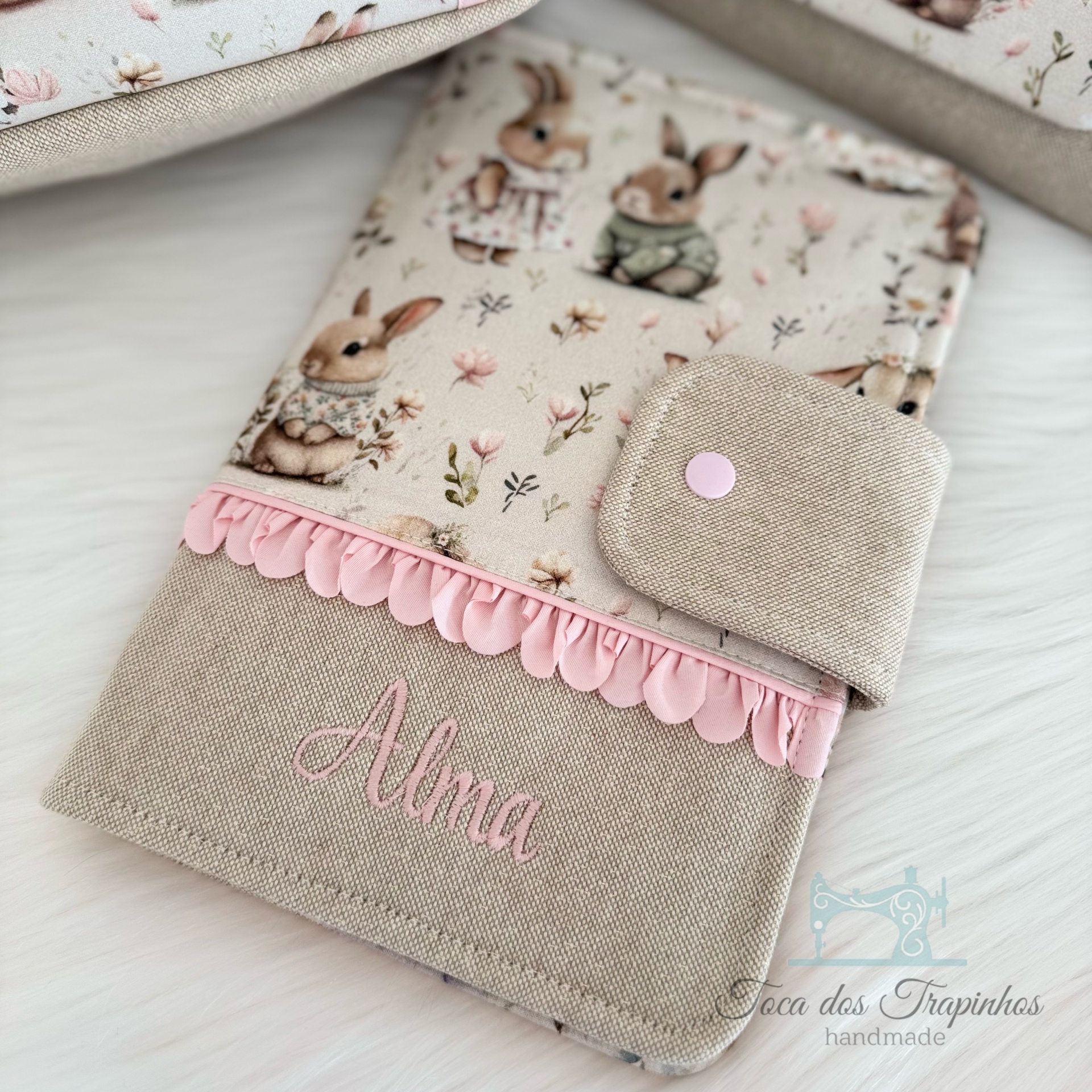 Capa em tecido com padrão de coelhinhos, bordado com nome Alma e detalhes em rosa