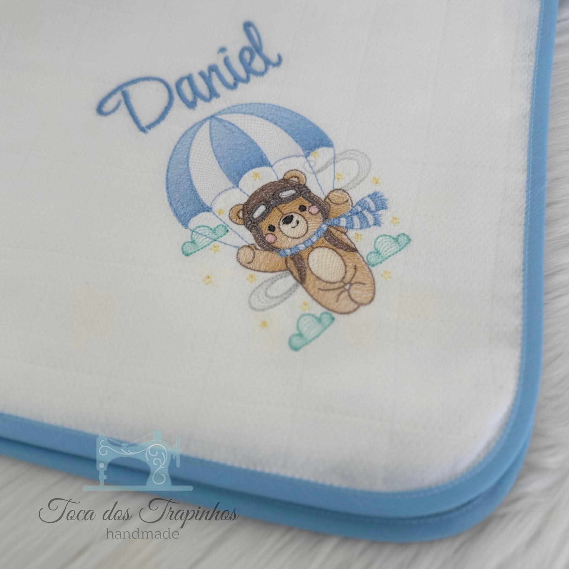 Fralda branca com borda azul e urso com paraquedas e nome Daniel bordados