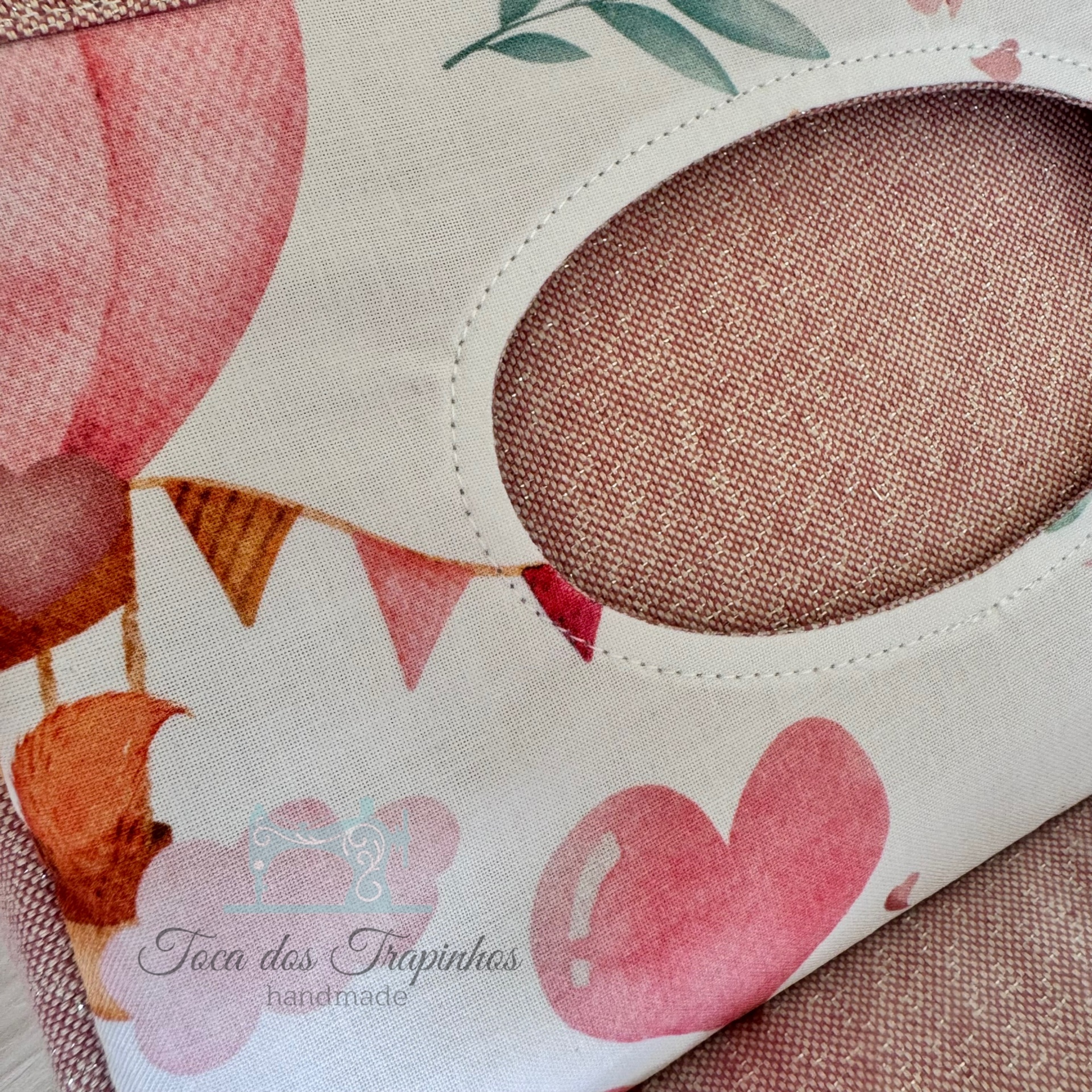 Capa de tecido rosa com padrão floral, recorte oval e texto artesanal