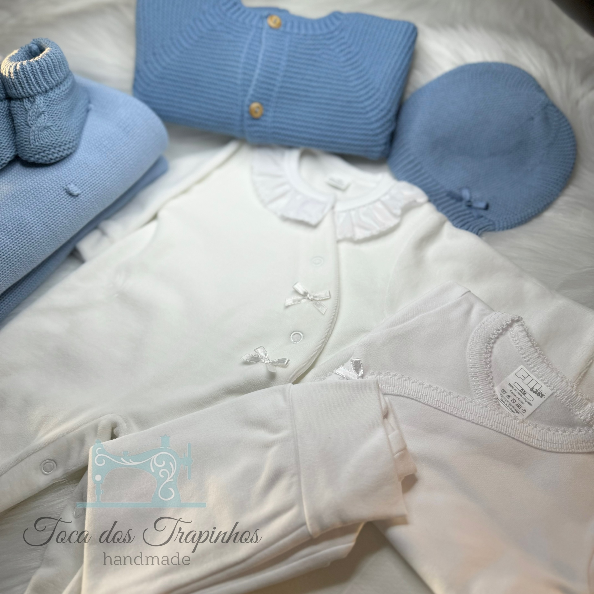 Conjunto de roupas de bebé azul e branco feitas à mão sobre superfície branca