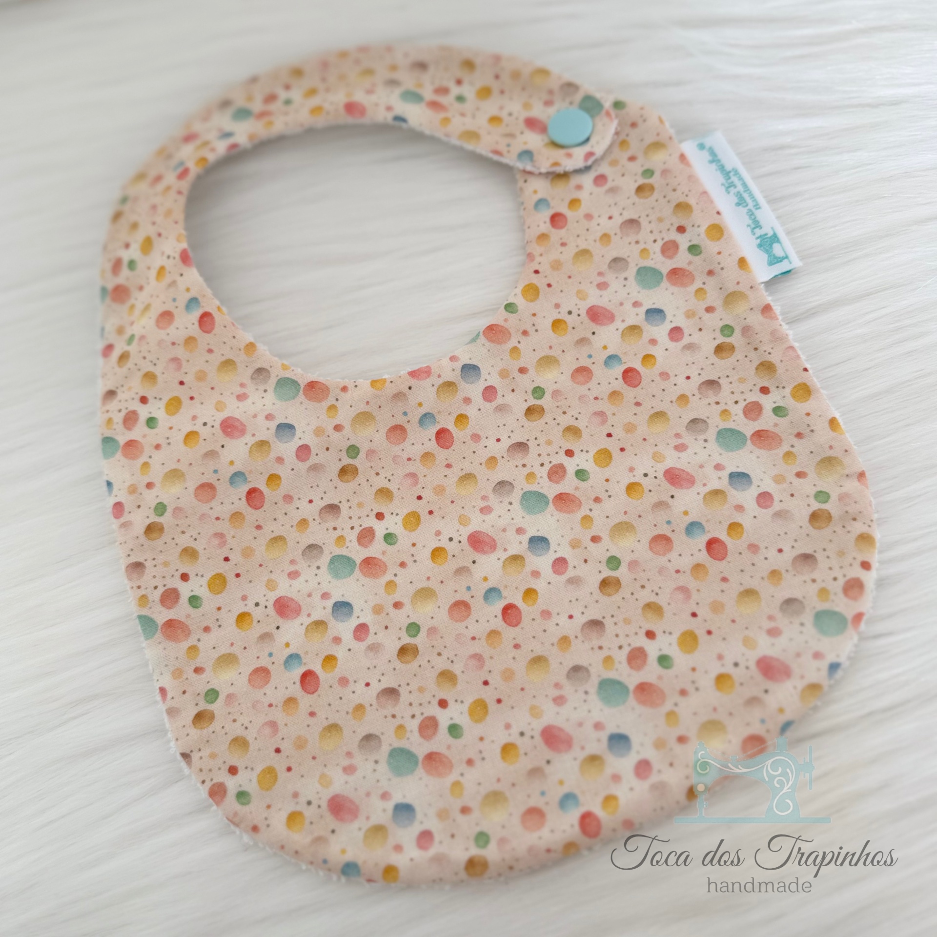 Babete para bebé com padrão de bolinhas coloridas e fecho de botão azul