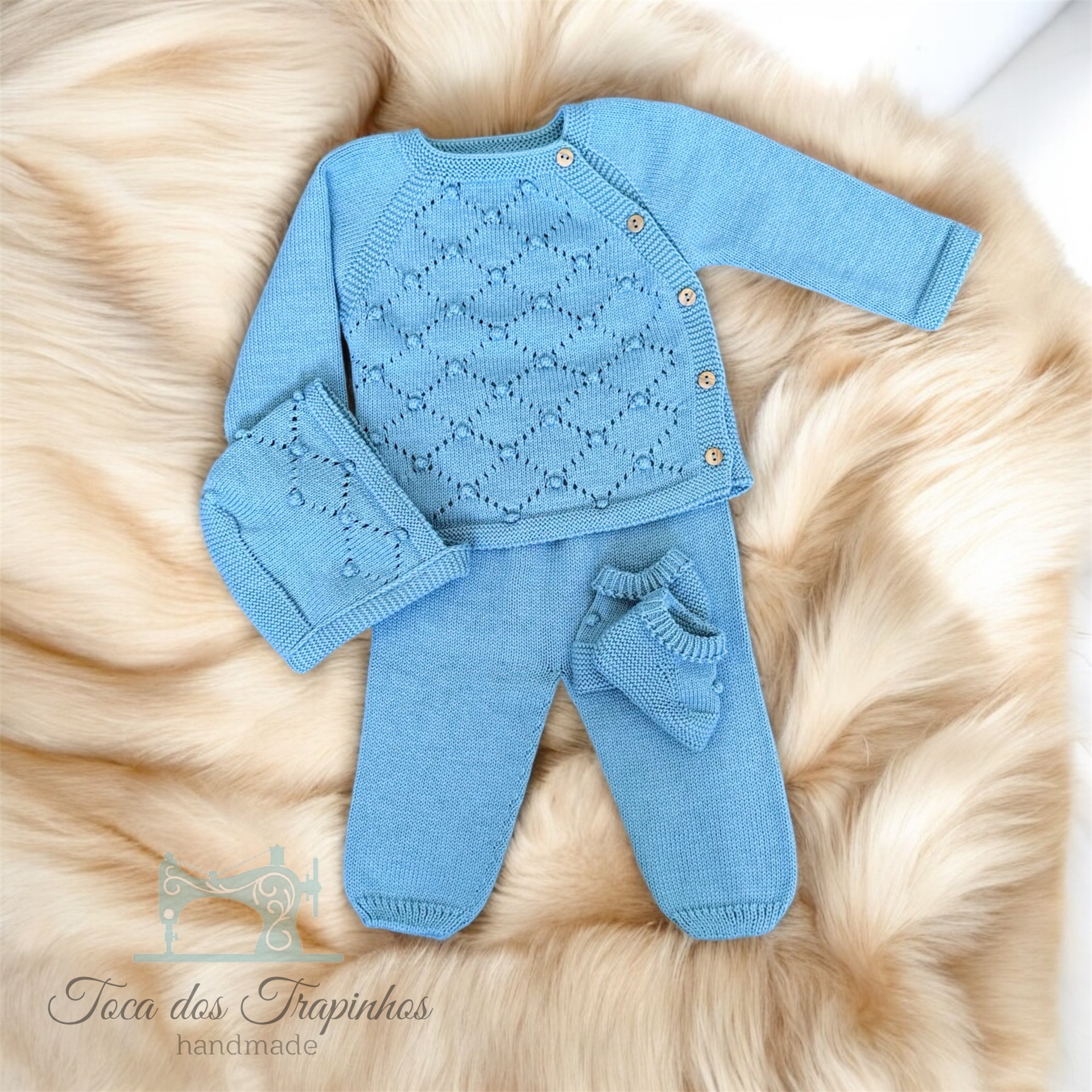 Conjunto de bebé azul em malha com casaco, calças, gorro e botinhas sobre pele sintética