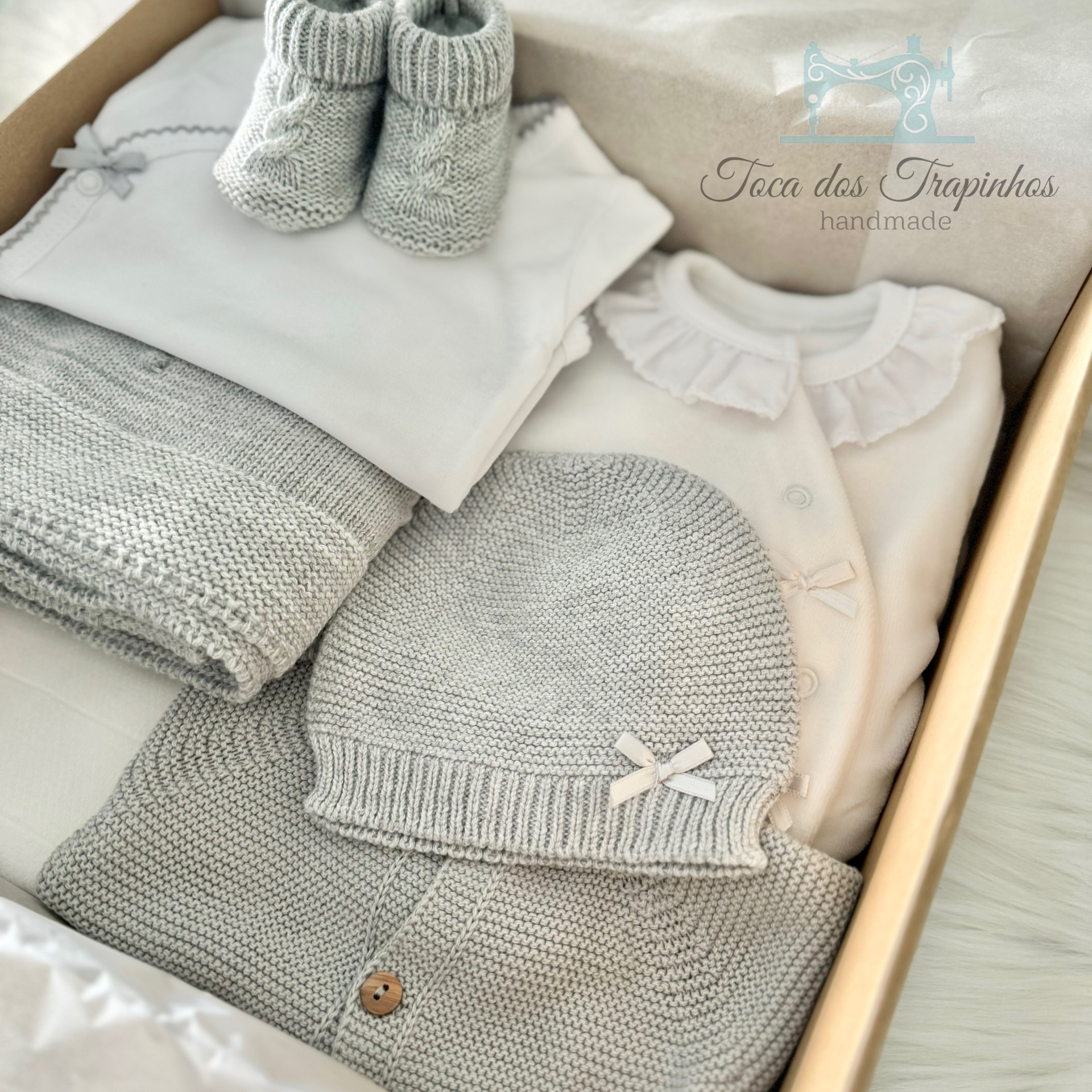Conjunto de roupa de bebé cinzenta e branca em caixa com logo 'Toca dos Trapinhos handmade'