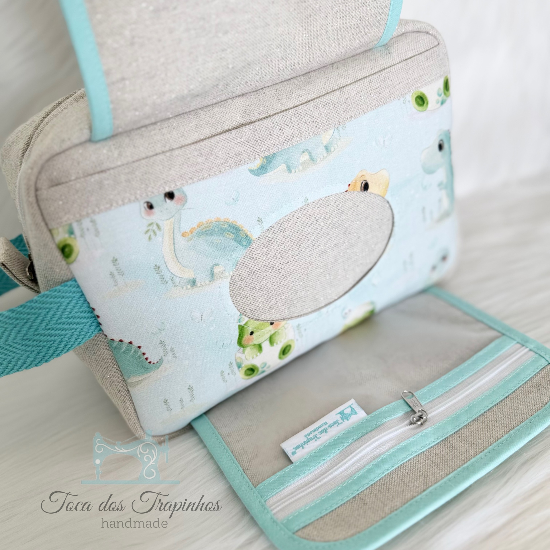 Bolsa infantil de tecido com padrão de dinossauros azul claro e detalhes bege e turquesa