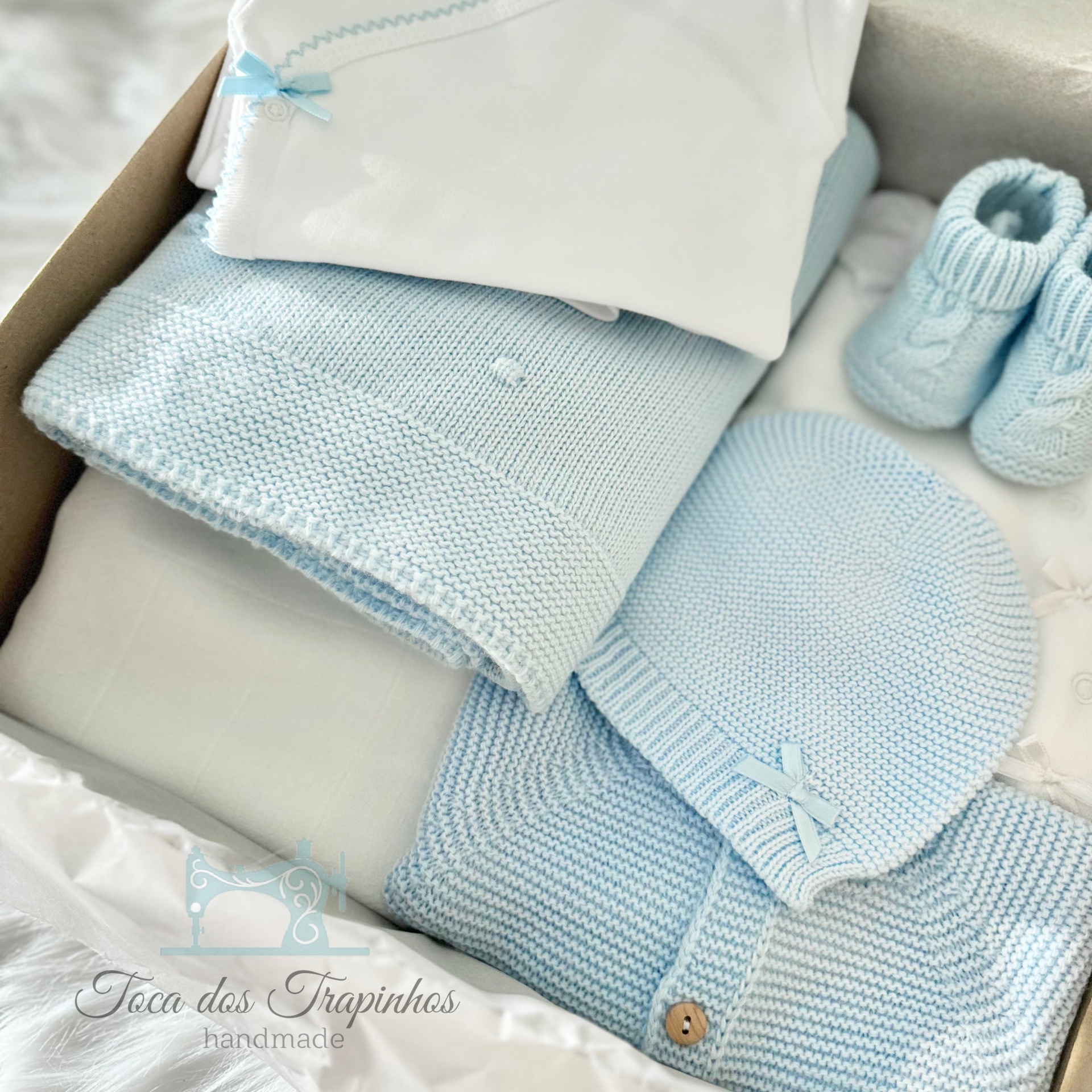 Conjunto de roupa de bebé azul claro em tricô numa caixa