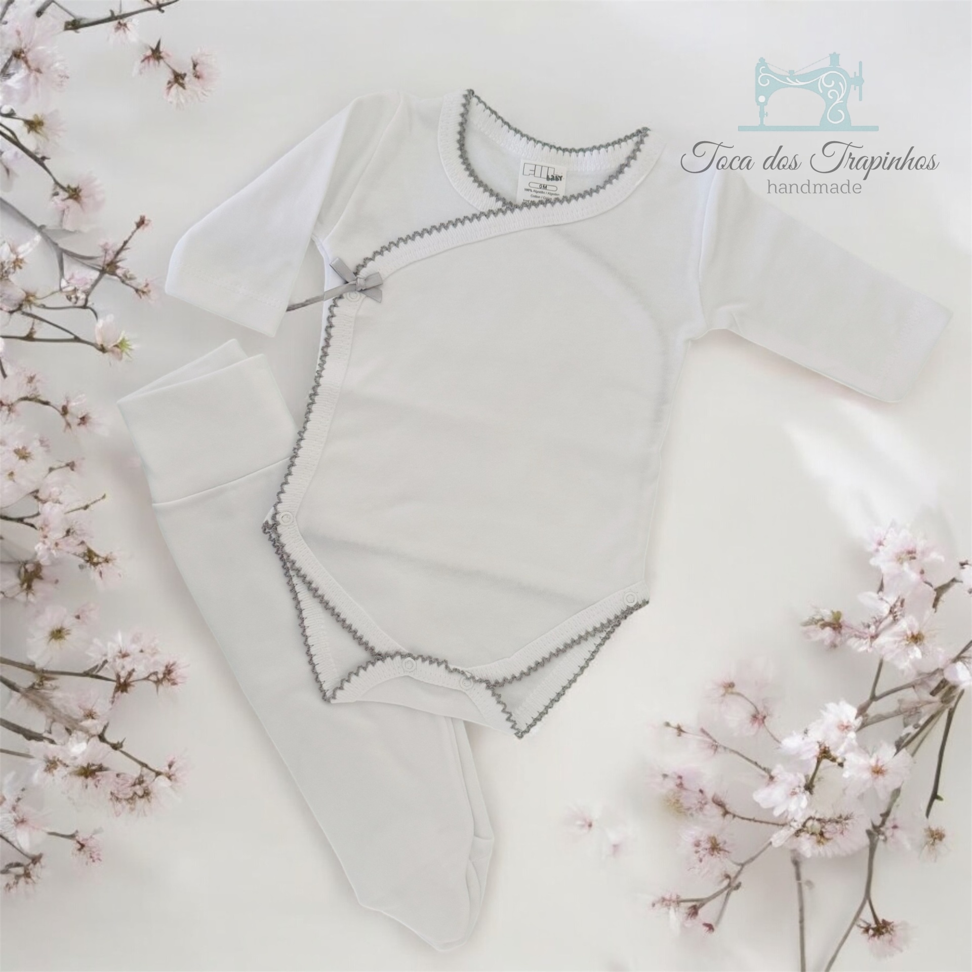 Conjunto de roupa de bebé branco com bordos cinzentos e laço, em fundo branco com flores rosas