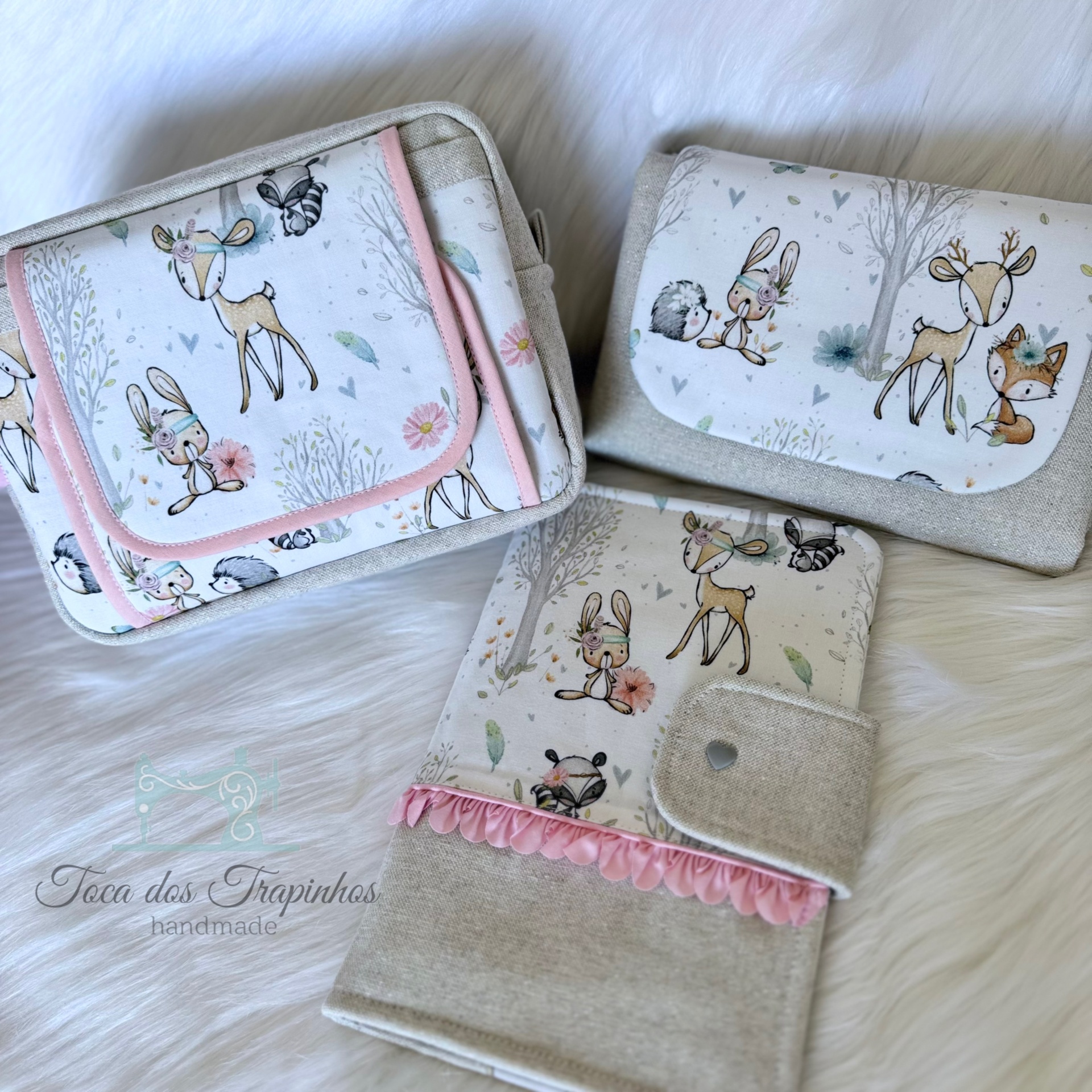 Conjunto artesanal de bolsa muda-fraldas, porta-fraldas e caderno de saúde com tecido estampado de animais da floresta e detalhes em rosa e bege.