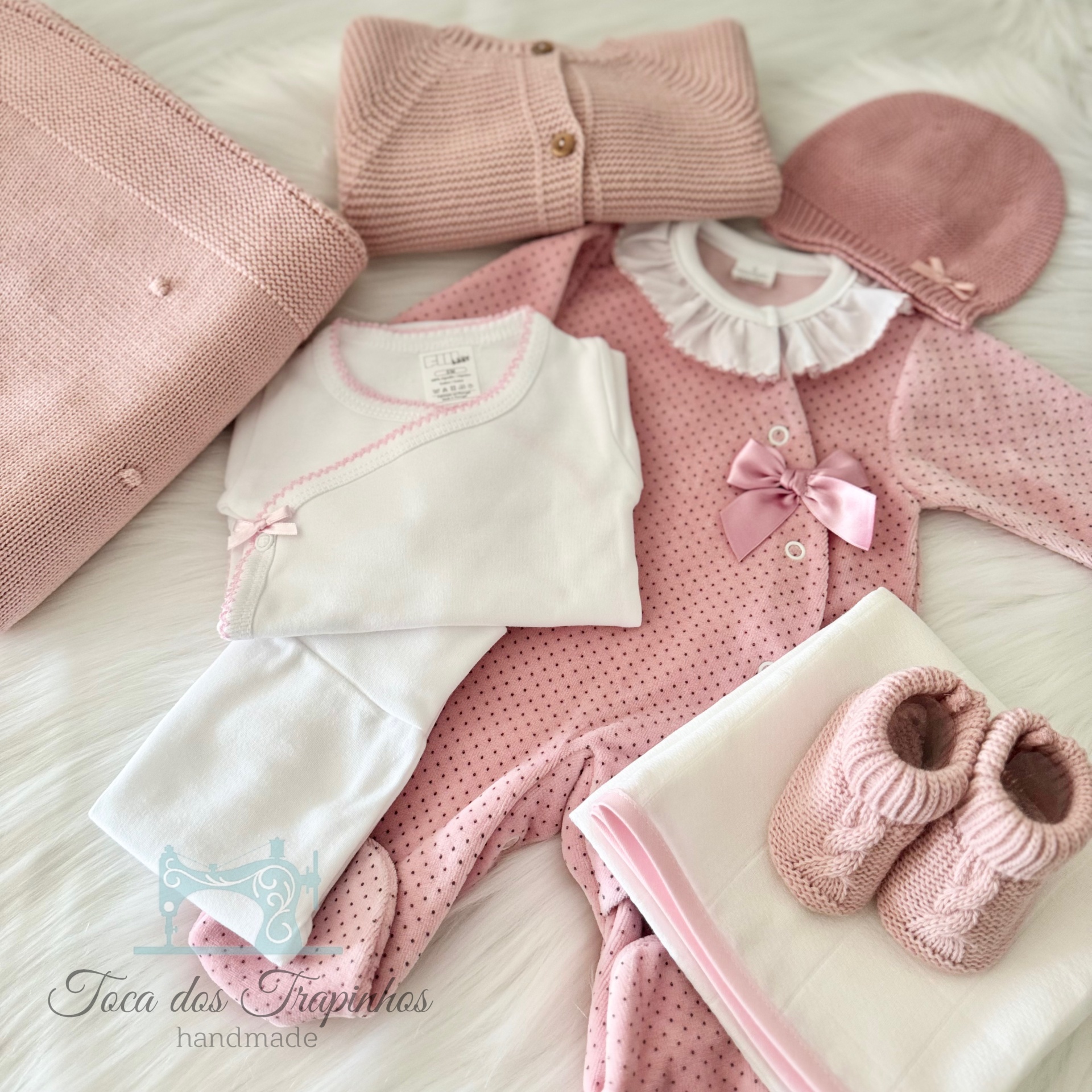 Conjunto de roupa de bebé rosa e branca com acessórios sobre superfície branca